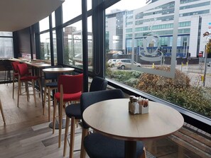 A modern cafe with large windows, wooden tables, and red chairs.