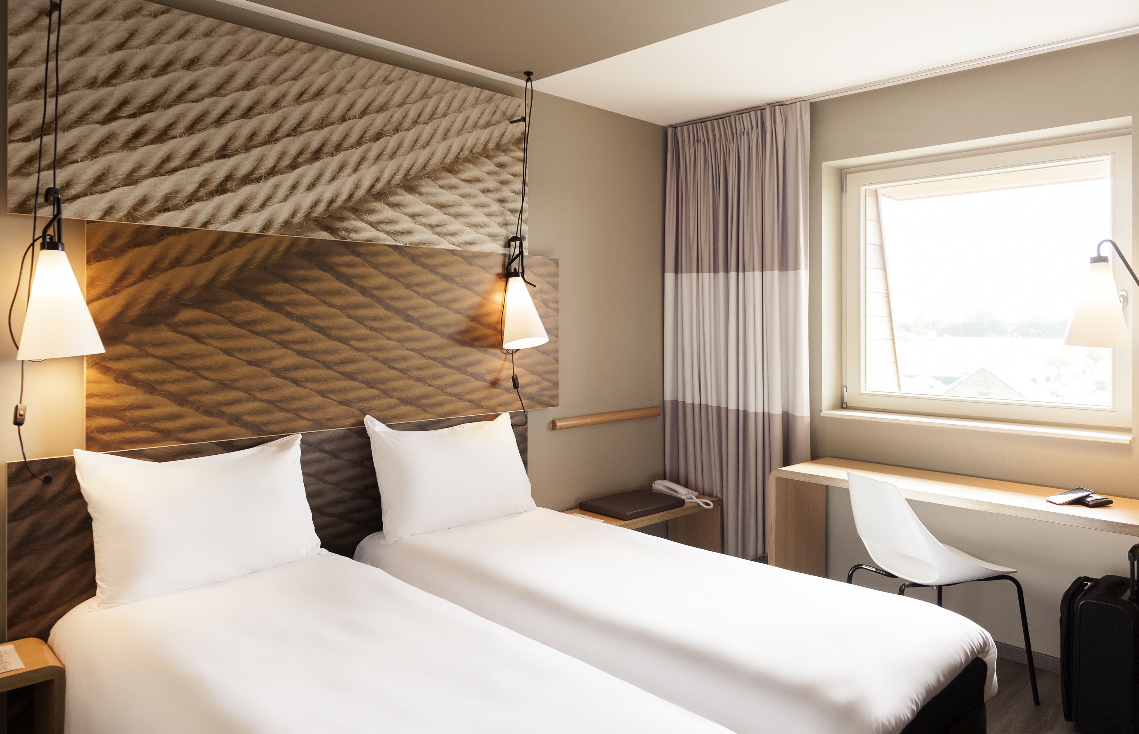 Ein Hotelzimmer mit Bett, Nachttischen, Schreibtisch, Stuhl und einem Fenster mit Vorhängen.