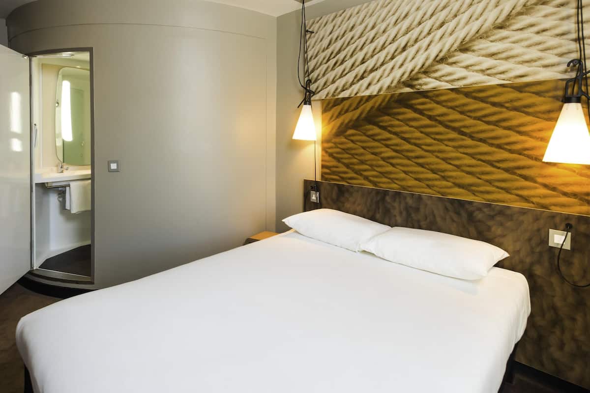 Habitación de hotel con cama, espejo, lavamanos y pared con un diseño texturizado.
