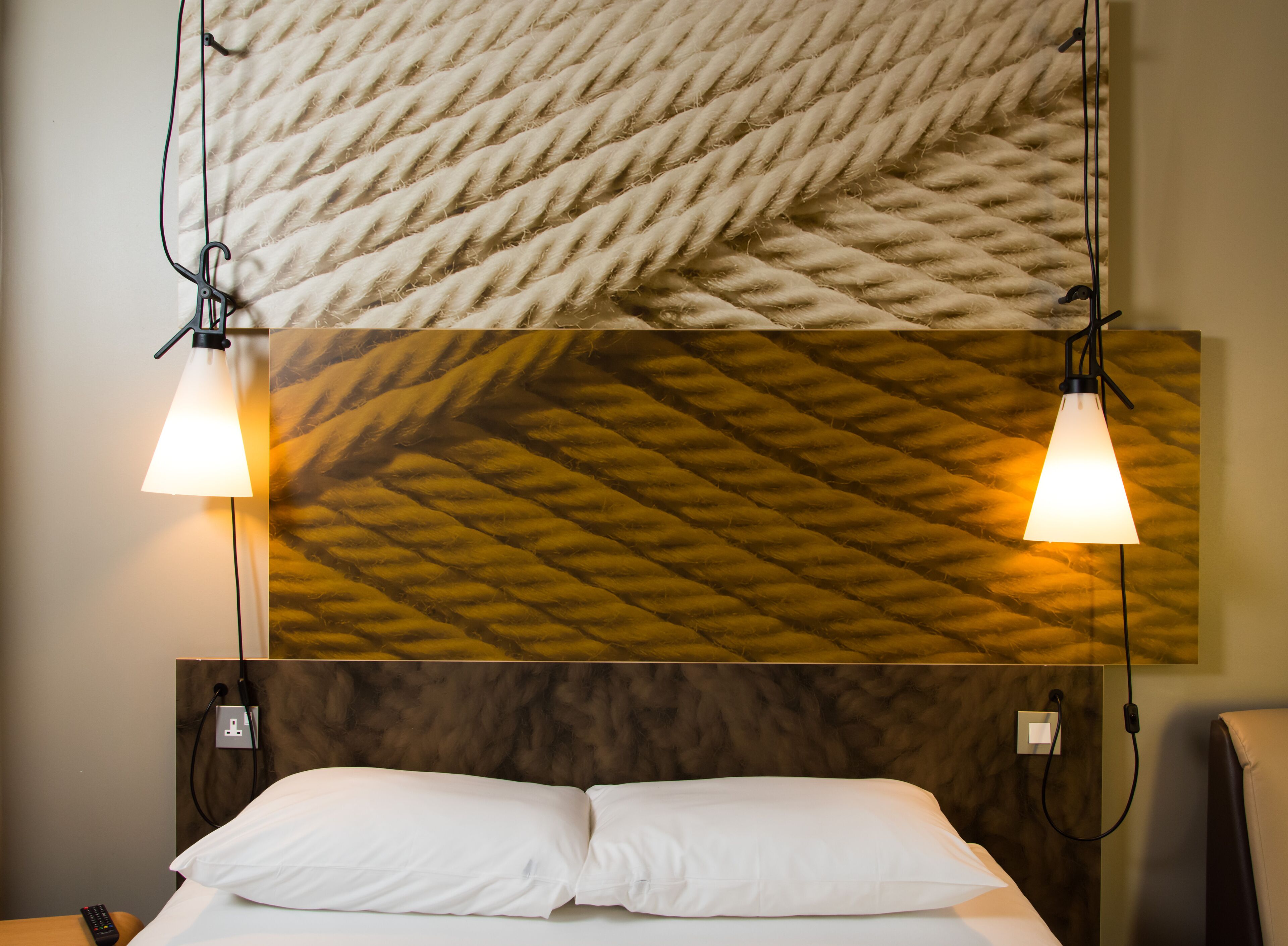 Una habitación de hotel con una cama, dos lámparas de noche, una lámpara de pared y un enchufe en la pared.