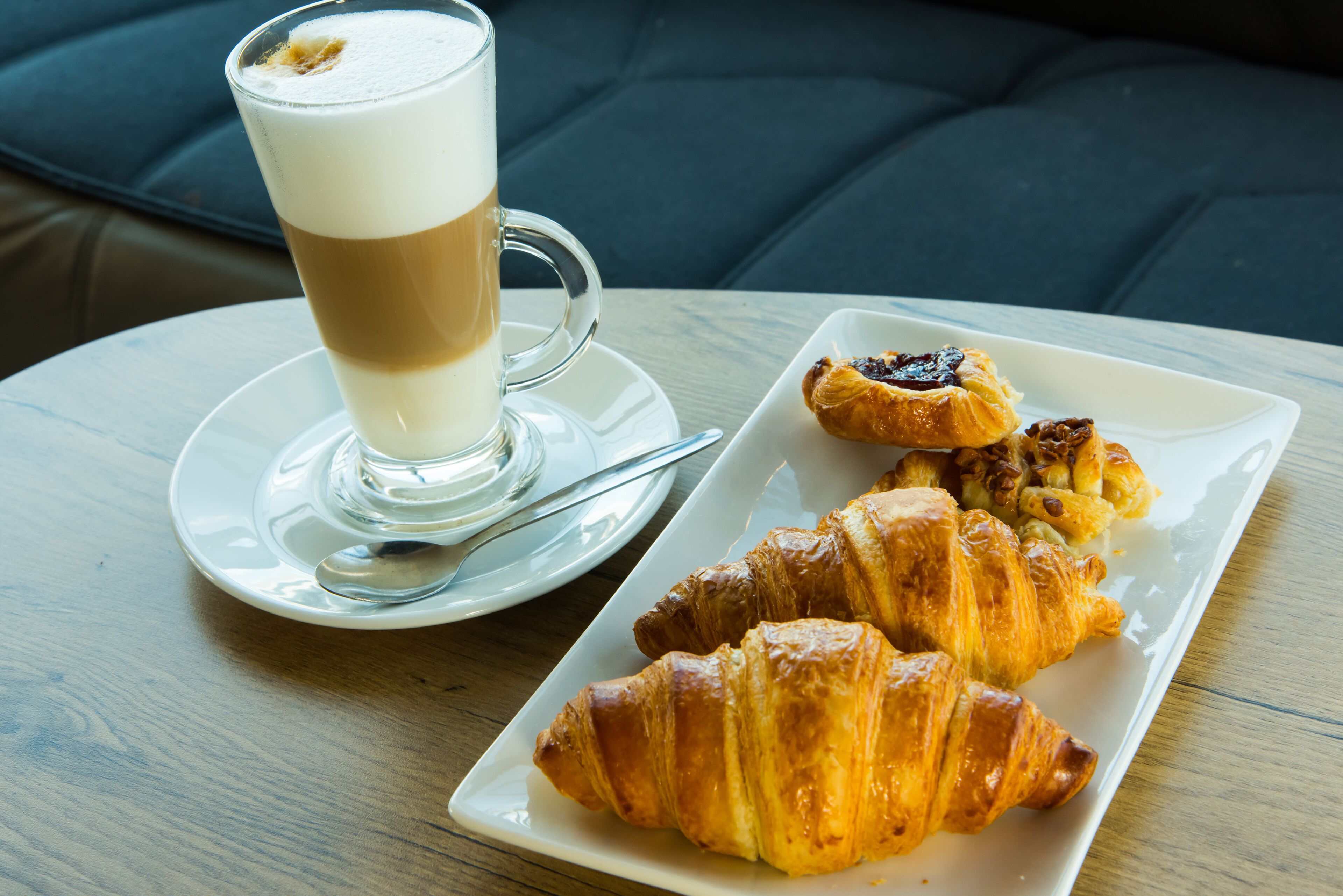 A table with a glass of coffee and a plate of croissants.