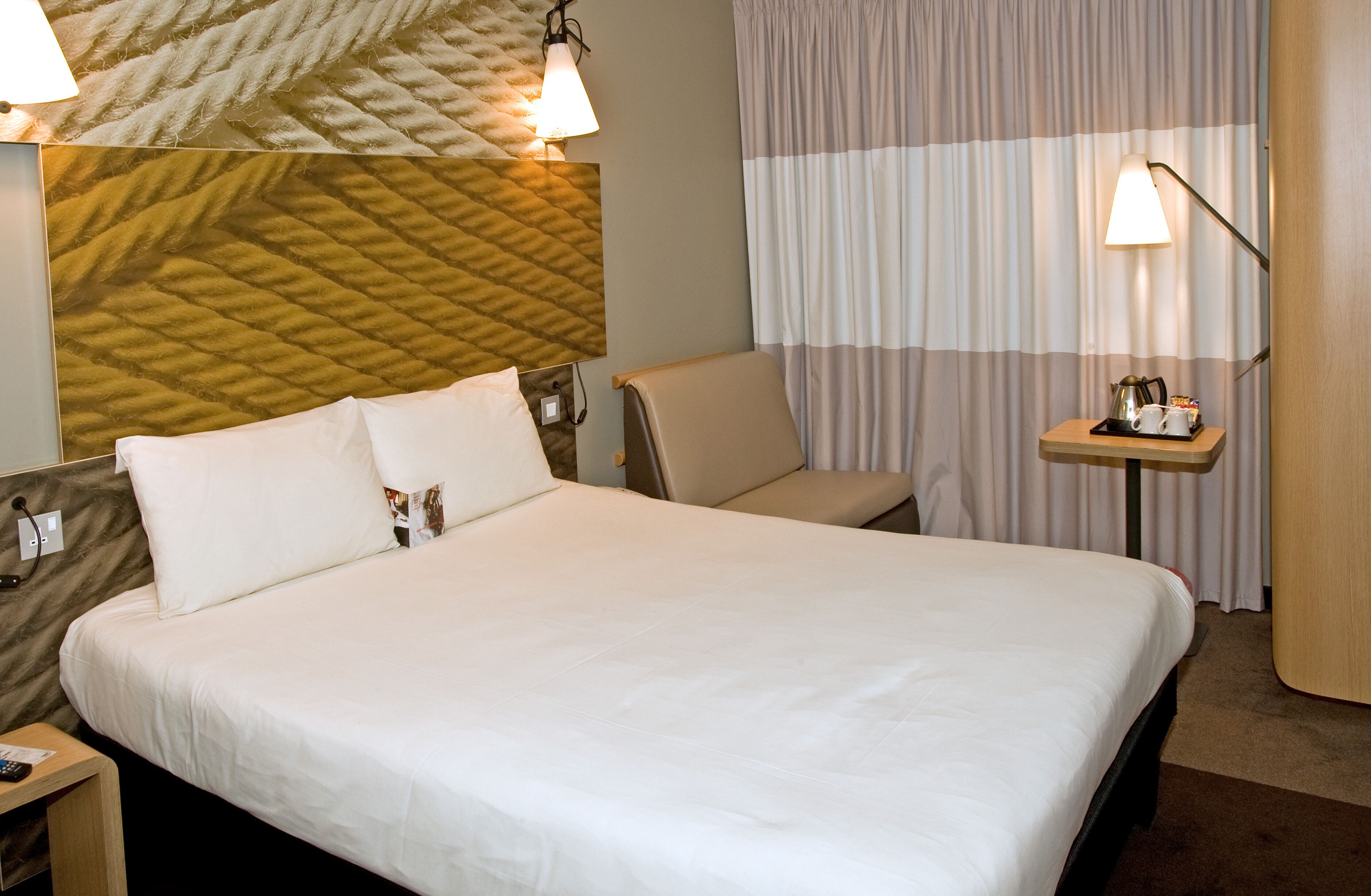 A neatly made bed with white linens, a bedside table with a lamp, and a wall with a textured pattern.