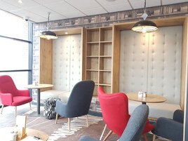 A modern lounge area with red and grey chairs, a wooden bookshelf, and pendant lighting.