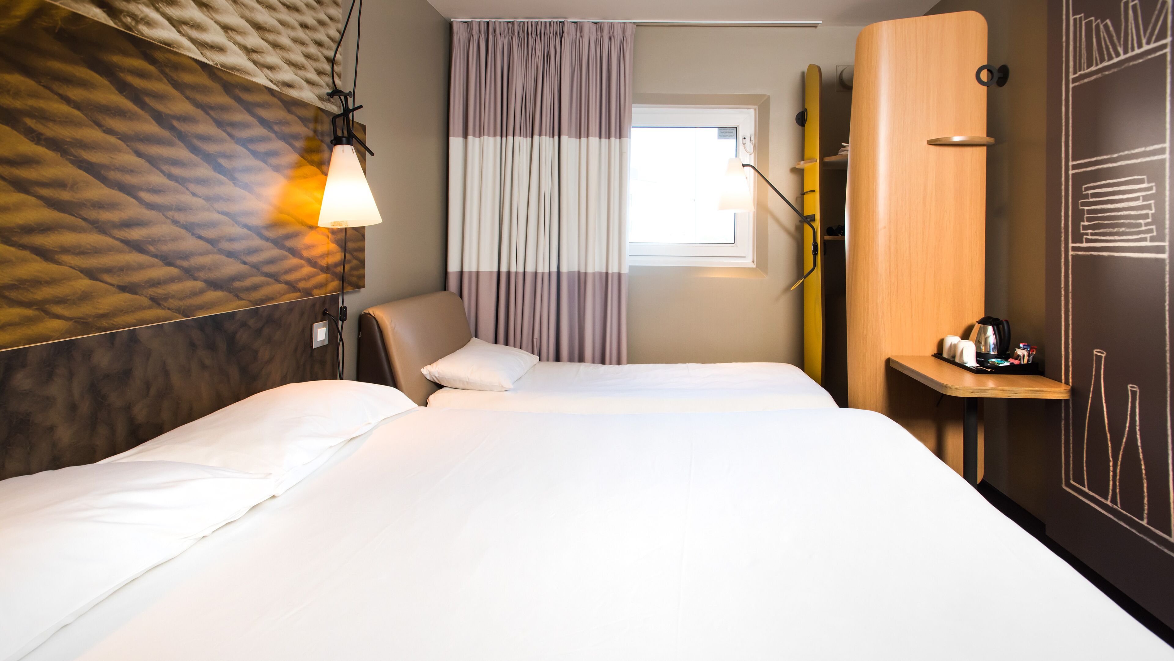 A hotel room with a bed, a chair, a desk, and a wardrobe.