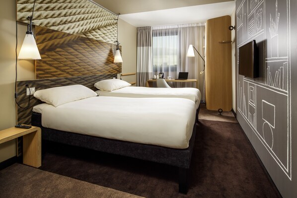 Een hotelkamer met twee bedden, een bureau met een laptop, een televisie en een kamer met een patroon op de muur.