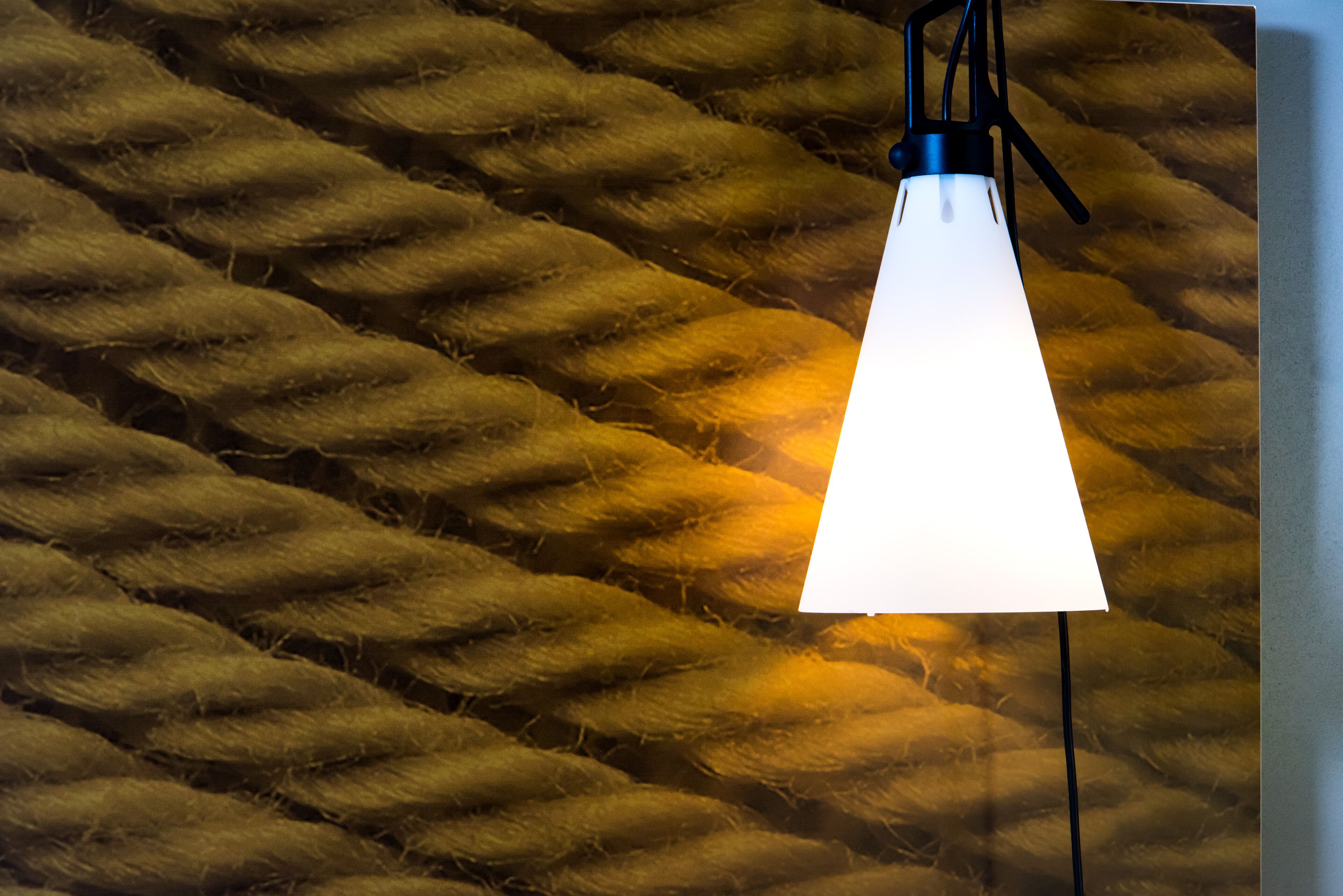 En hänglampa med en vit lampskärm, placerad framför en vägg med en tydlig struktur.