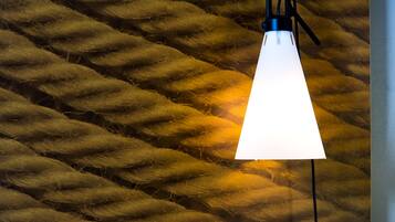 En hänglampa med en vit lampskärm, placerad framför en vägg med en tydlig struktur.