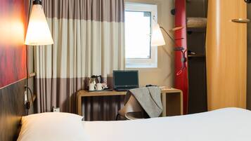 Habitación de hotel con cama, escritorio con una computadora portátil, una tabla de surf roja y una ventana con cortinas.