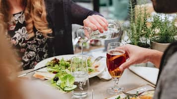 A dining table with plates of food, glasses, and a person pouring a drink.