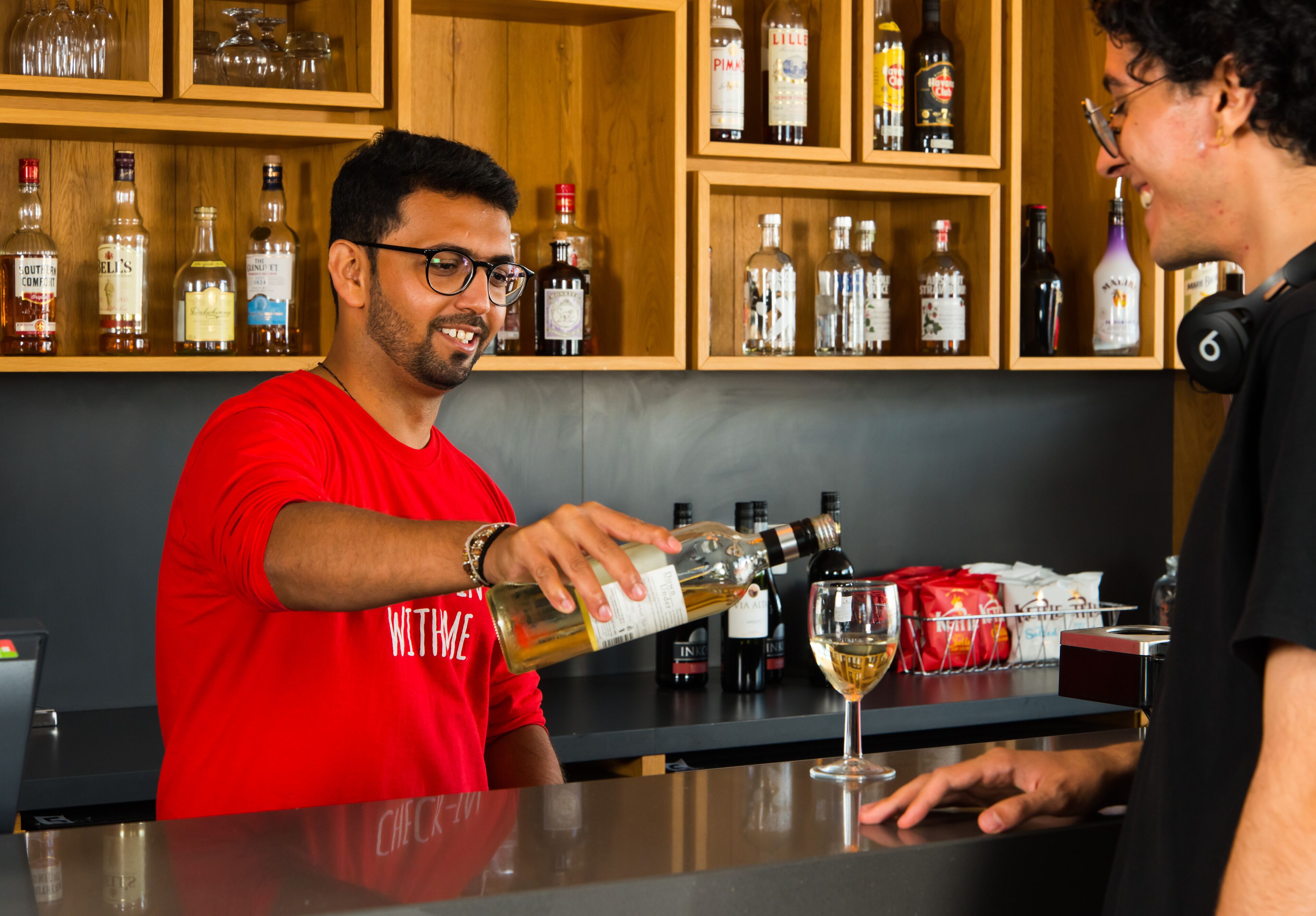 Zona de bar con estantes llenos de botellas de licores y una persona sirviendo una bebida en un vaso.