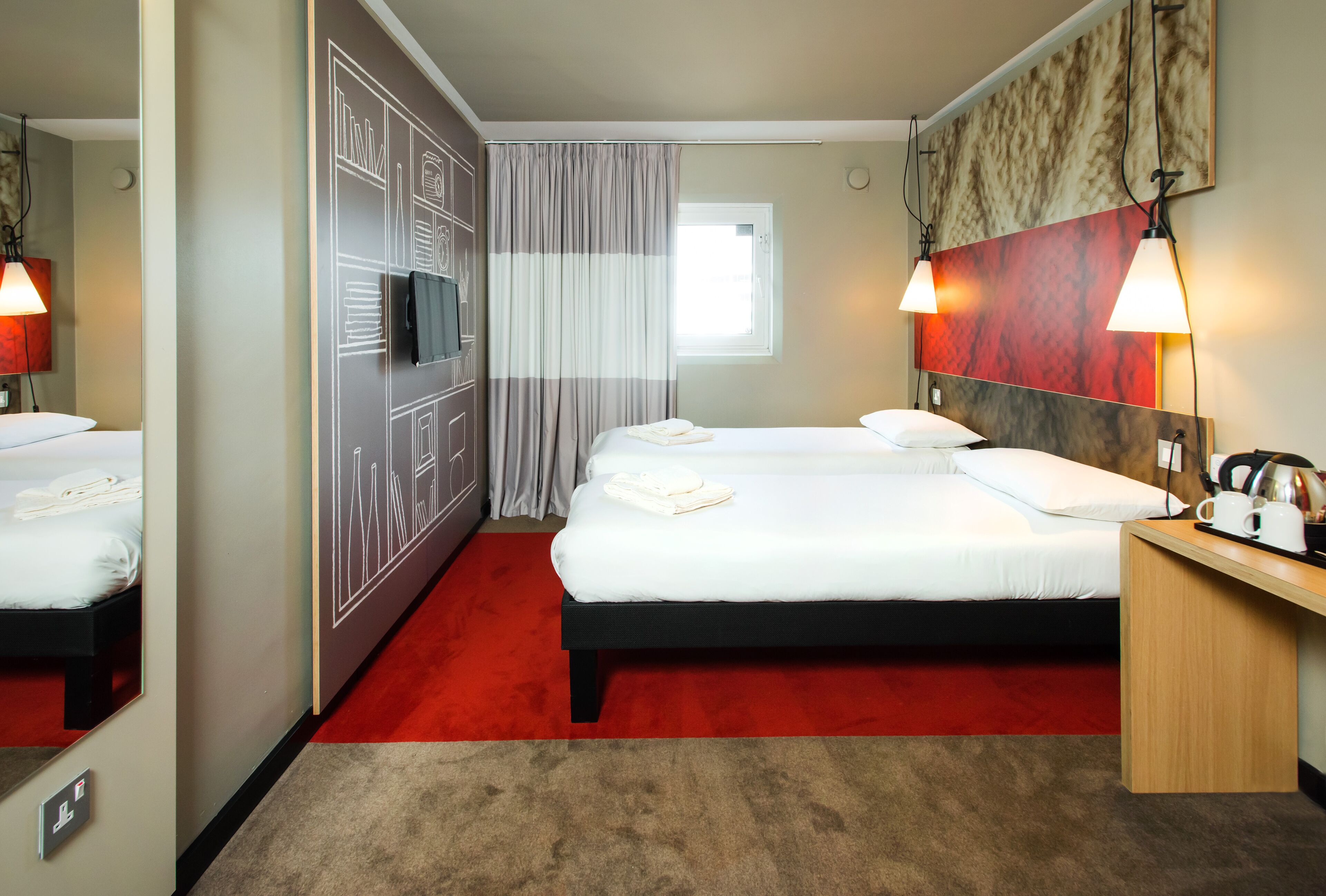 A hotel room with a large bed, a desk with a coffee maker, and a mirror.