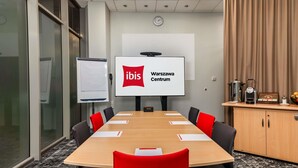 A conference room with a large table, red chairs, a whiteboard, a screen displaying 'ibis Warszawa Centrum,' and a coffee station. - ibis Warszawa Centrum (Warsaw)