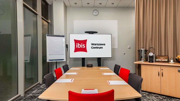 A conference room with a large table, red chairs, a whiteboard, a screen displaying 'ibis Warszawa Centrum,' and a coffee station. - ibis Warszawa Centrum (Warsaw)