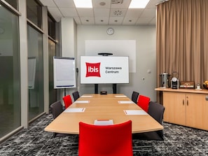 A conference room with a large table, red chairs, a whiteboard, a screen displaying 'ibis Warszawa Centrum,' and a coffee station. - ibis Warszawa Centrum (Warsaw)