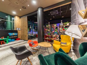 A modern interior with a wooden reception desk, colorful chairs, a bookshelf, and a large pillar. - ibis Warszawa Centrum (Warsaw)