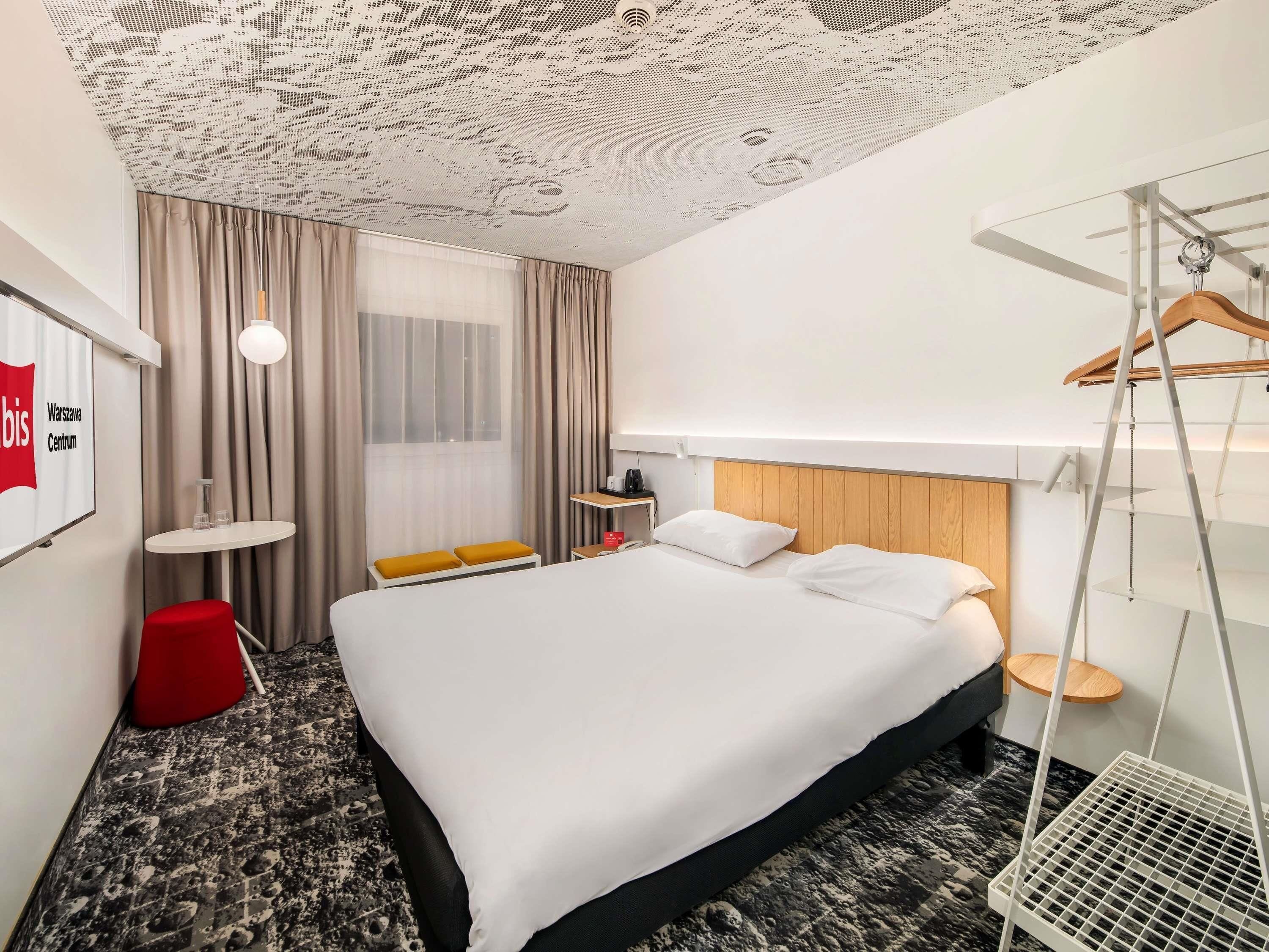 Une chambre d’hôtel avec un lit, un bureau, une chaise, un luminaire suspendu et une vue sur la ville.