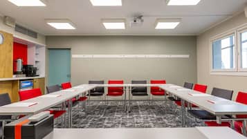 Un salón de conferencias con una larga mesa, sillas rojas y negras, un proyector y un reloj en la pared.