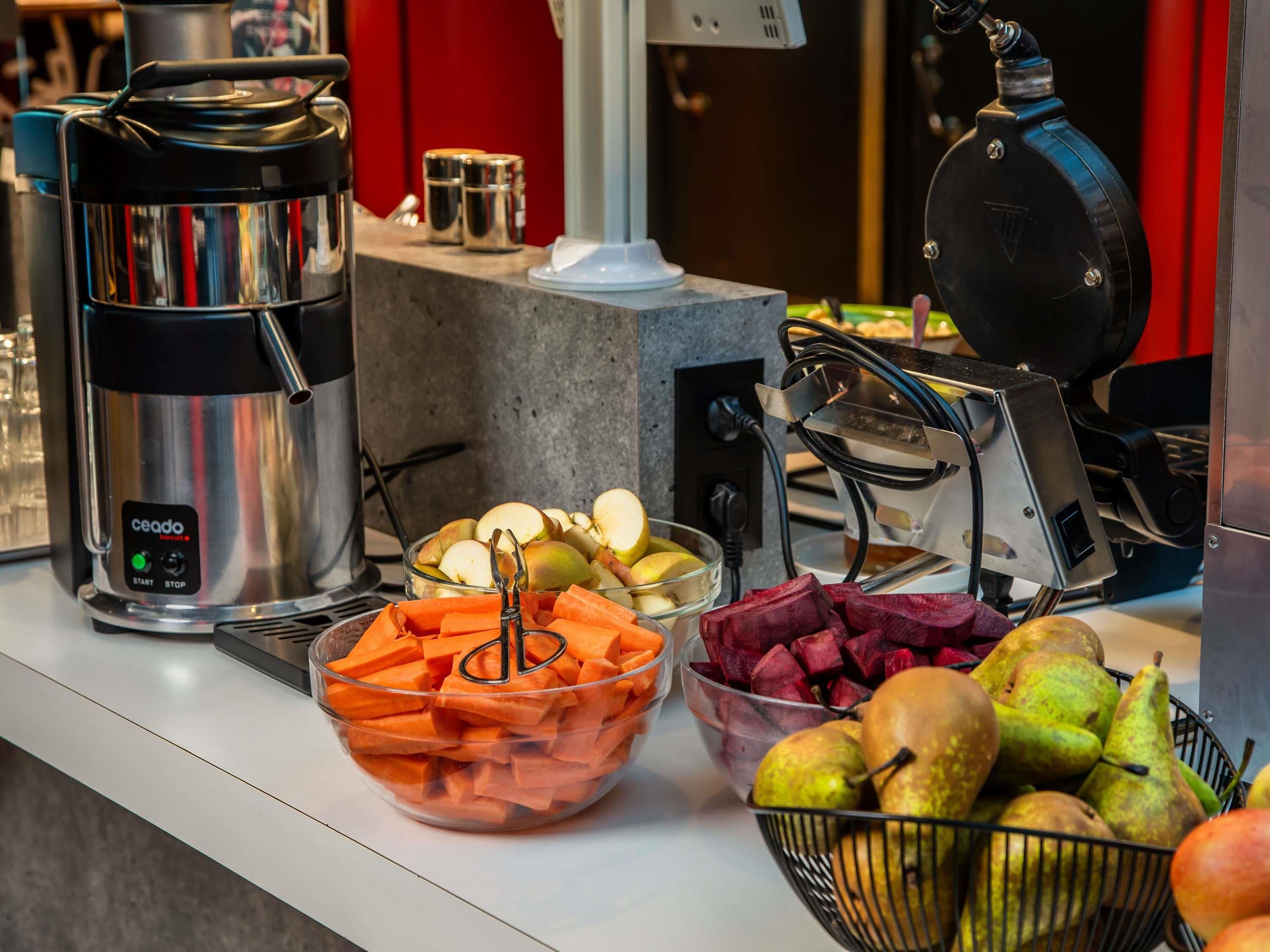 A buffet setup with a coffee maker, bowls of sliced fruits and vegetables, and a fruit basket.
