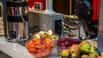 A buffet setup with a coffee maker, bowls of sliced fruits and vegetables, and a fruit basket.