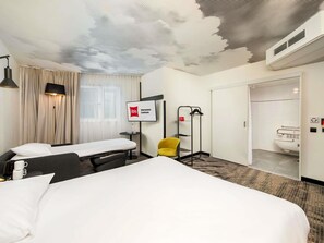 A hotel room with two beds, a TV, a chair, a coat rack, and a bathroom visible through an open door. - ibis Warszawa Centrum (Warsaw)
