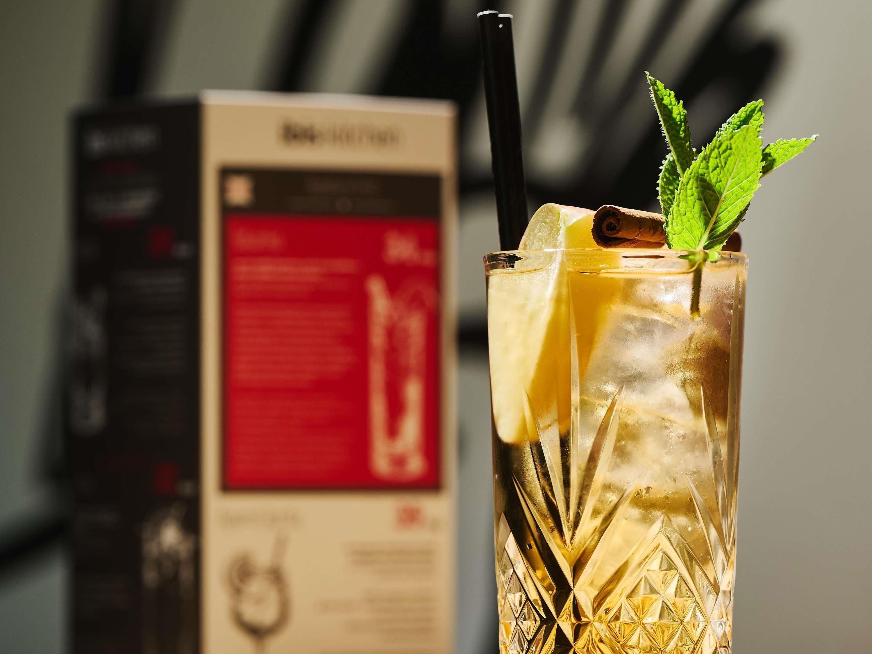 A glass with a straw, lemon slice, mint, and cinnamon stick, with a box in the background.
