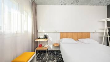 Une chambre d’hôtel avec un lit, une table de chevet avec une bouilloire, un téléphone et une petite table sur laquelle est posé un panneau rouge.