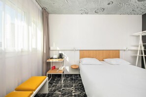 A hotel room with a bed, a bedside table with a kettle, a telephone, and a small table with a red sign. - ibis Warszawa Centrum (Warsaw)