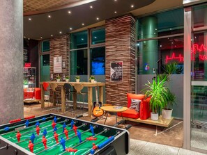 A modern indoor space with a foosball table, seating area, and a wall with a poster. - ibis Warszawa Centrum (Warsaw)