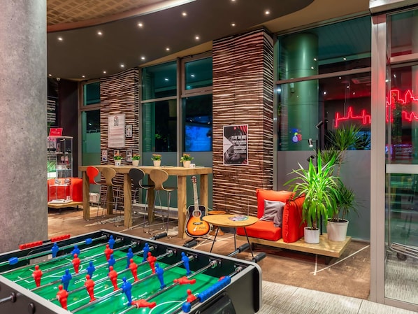 A modern indoor space with a foosball table, seating area, and a wall with a poster. - ibis Warszawa Centrum (Warsaw)