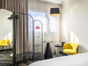 A hotel room with a bed, two yellow chairs, a small table with a lamp, and a glass shelf unit. - ibis Warszawa Centrum (Warsaw)