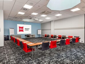 A conference room with a long table, red and black chairs, a whiteboard, and a screen displaying 'ibis Warszawa Centrum'. - ibis Warszawa Centrum (Warsaw)