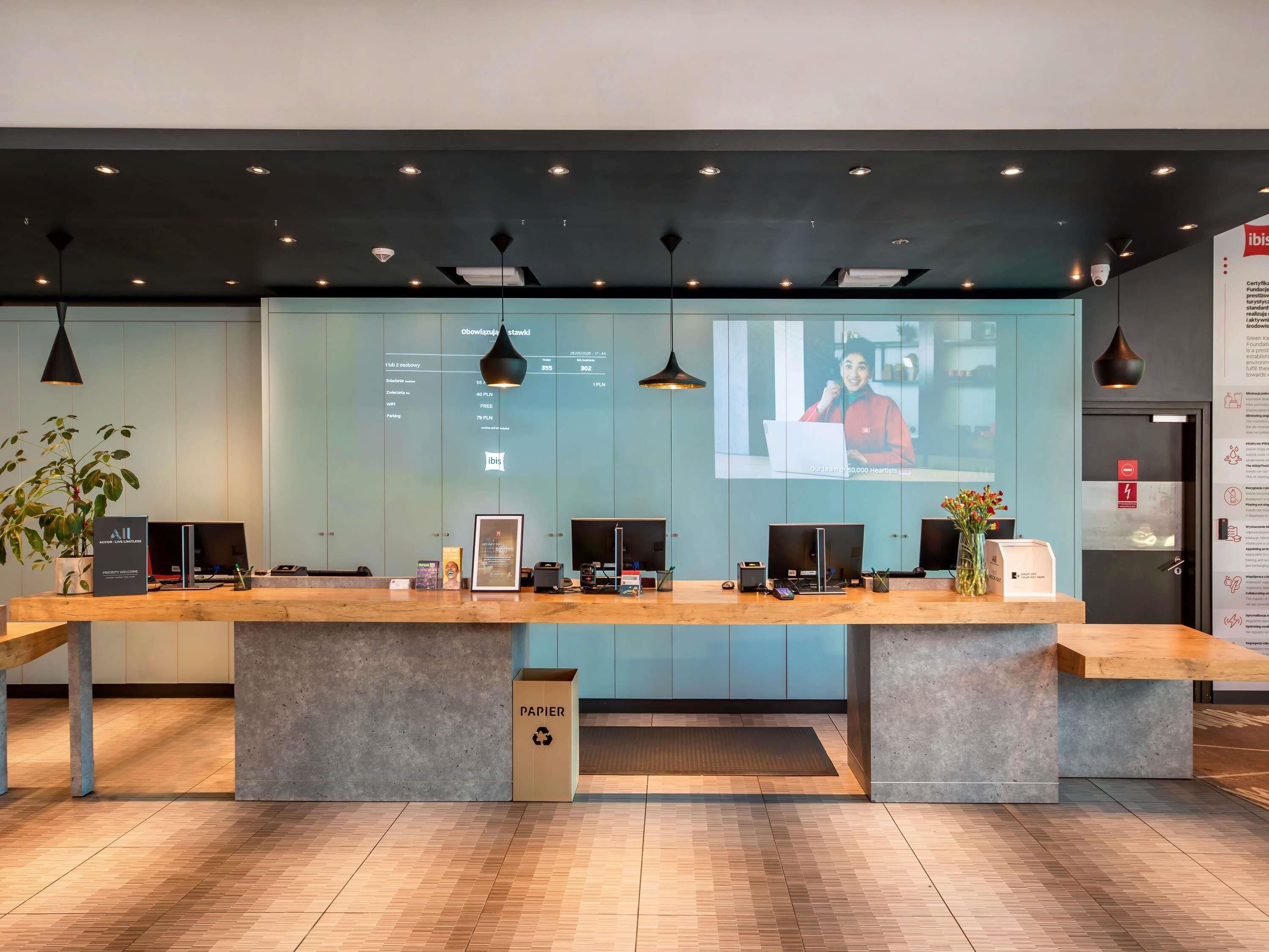 Un mostrador de recepción con una computadora, una planta y un contenedor de reciclaje.