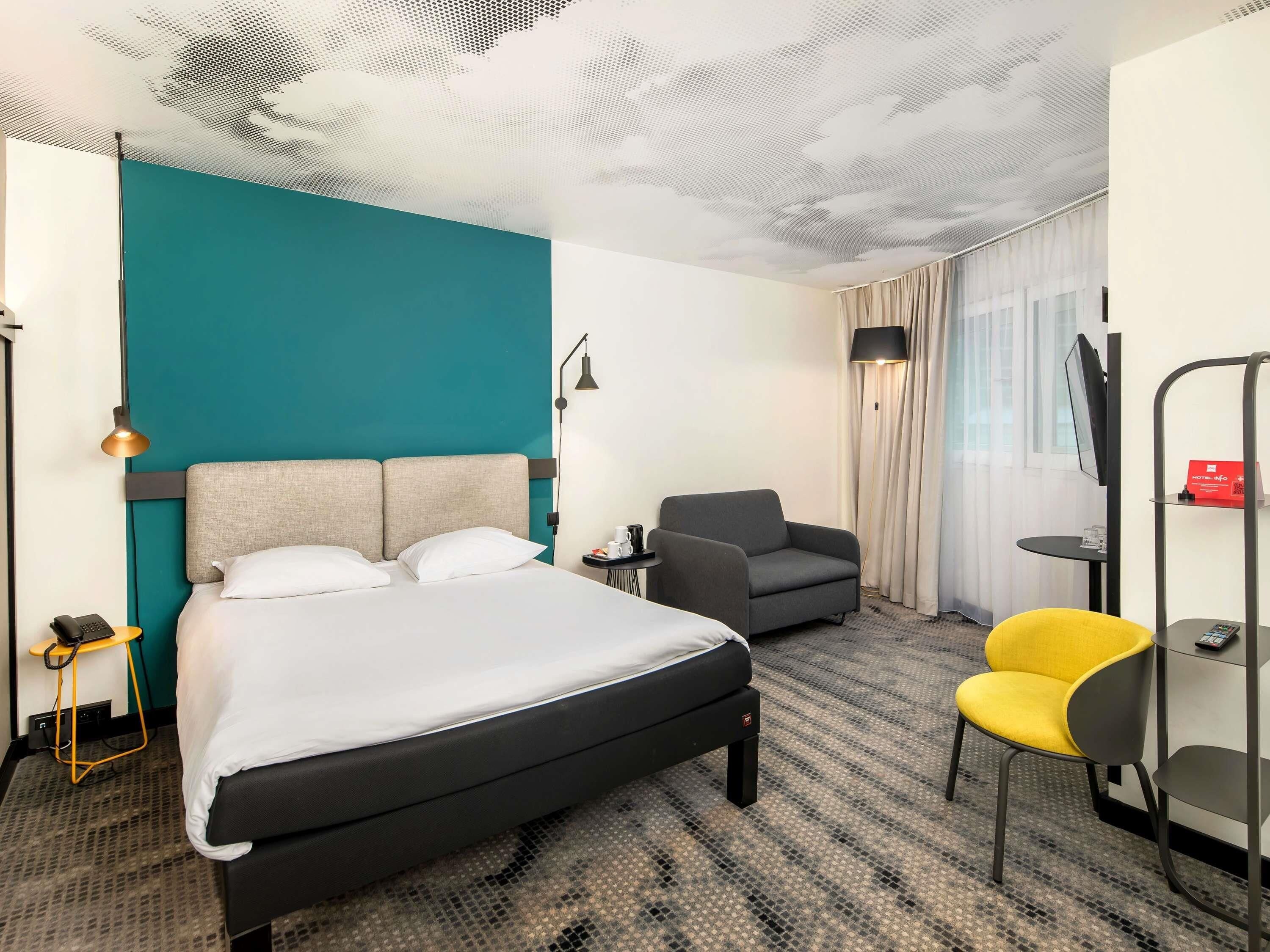 Habitación de hotel con una cama, una silla, un escritorio y un televisor.