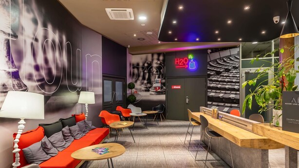 Et moderne loungeområde med siddepladser, en reception og et neonlys, der viser vejen til en vanddispenser.