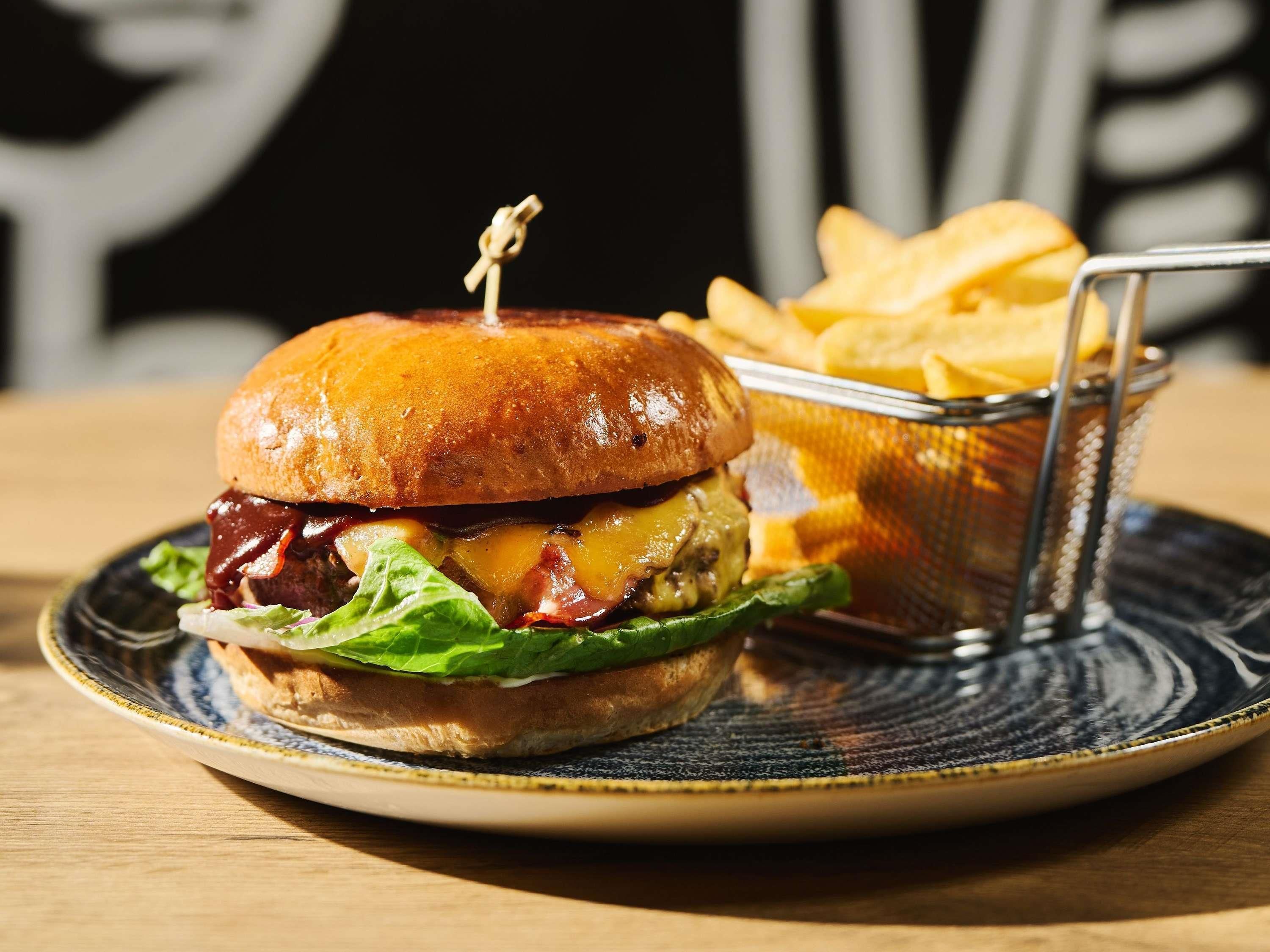 En hamburgare med en tandpetare på toppen, sallad, ost och ett bröd, serverad på en tallrik med en portion pommes frites som tillbehör.