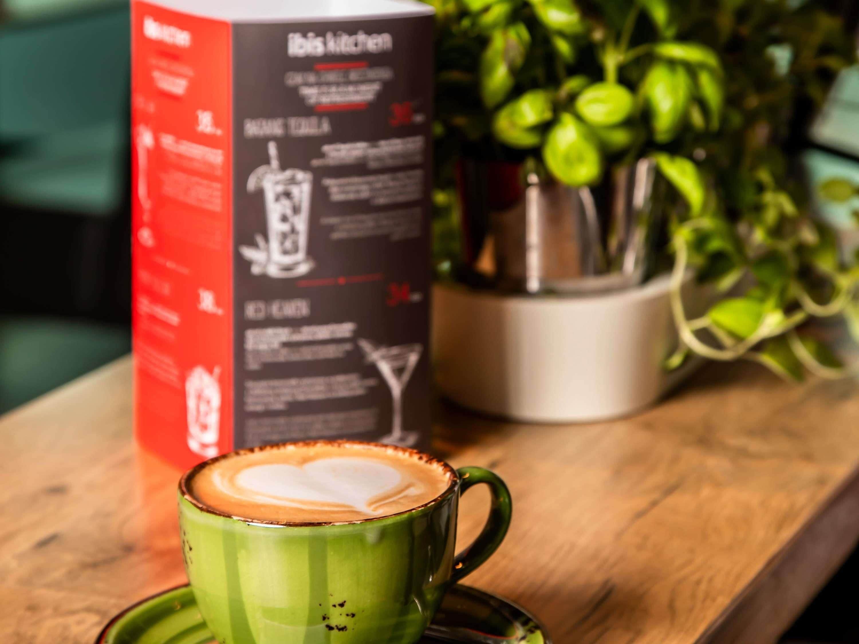 A green coffee cup with latte art on a saucer, a box labeled 'Robis Kitchen,' and a potted plant in the background.