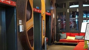 A hotel lobby with a red sofa, a whiteboard, and a large wooden sculpture. - ibis Warszawa Centrum (Warsaw)