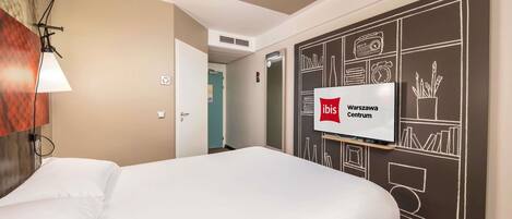 A hotel room with a bed, a wall-mounted TV, and a red carpet.