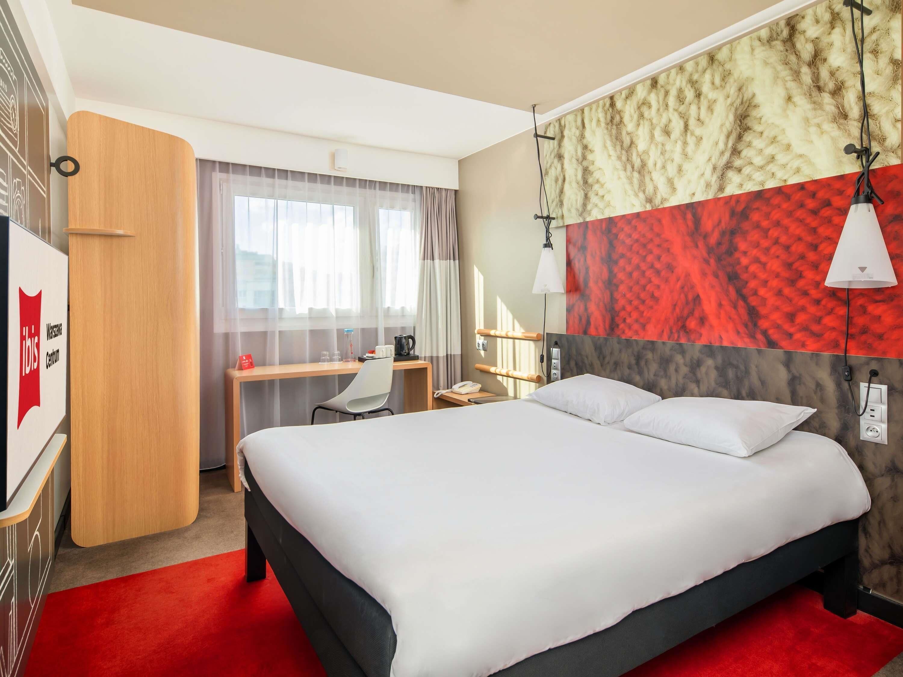 A hotel room with a bed, desk, chair, and a view of the city.