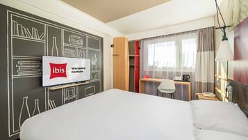 Una habitación de hotel con una cama, un escritorio, una silla, un televisor y un armario.