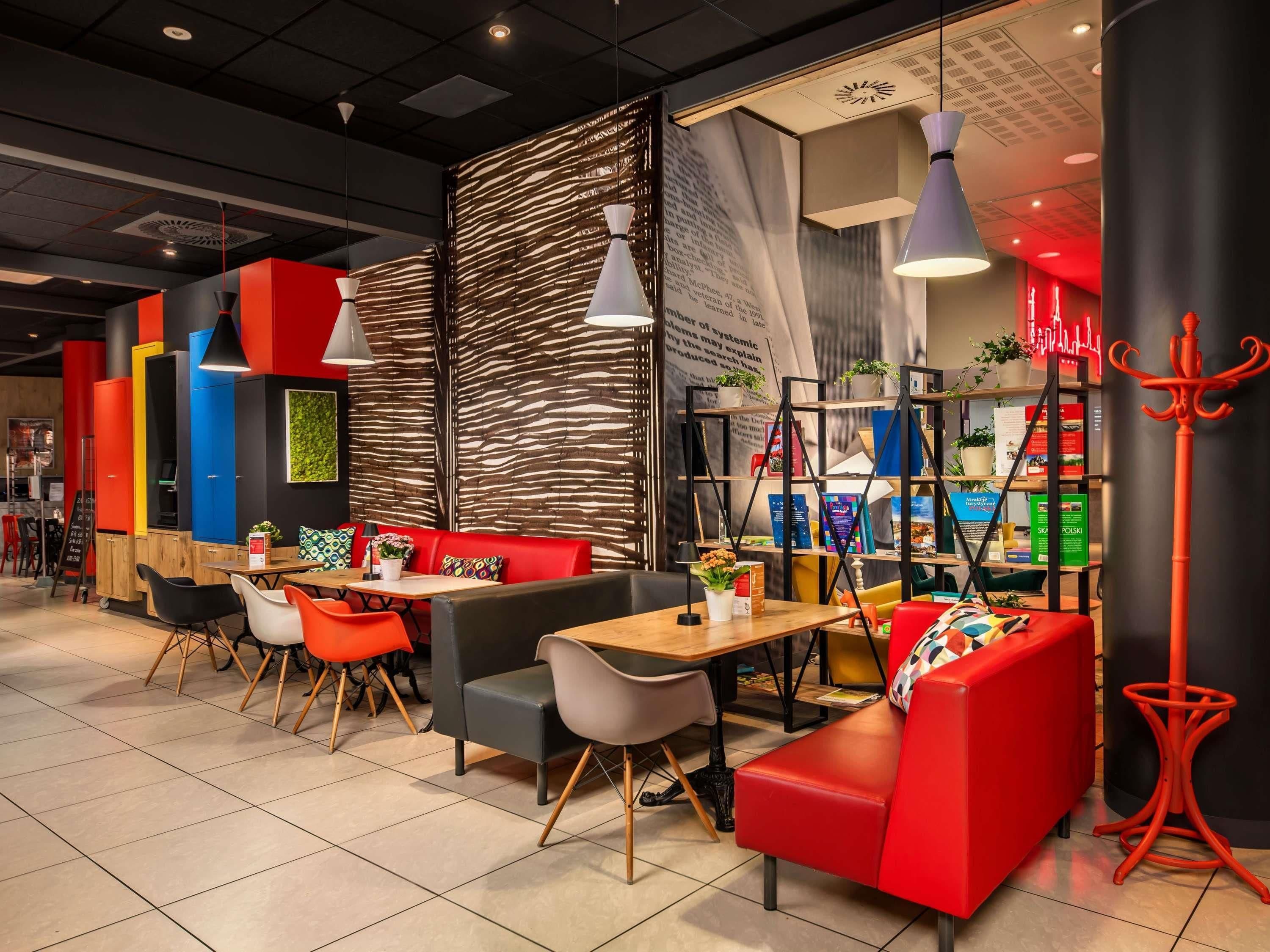 A modern cafe interior with red and black seating, wooden tables, and a variety of plants.
