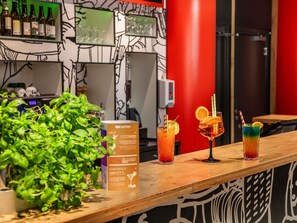 A bar area with a counter displaying three drinks, a potted plant, and a menu box. - ibis Warszawa Centrum (Warsaw)