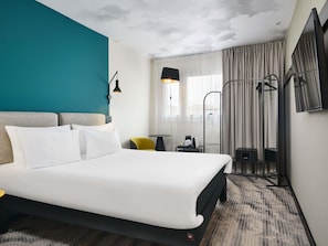 A hotel room with a bed, a desk, a chair, a TV, and a window with curtains. - ibis Warszawa Centrum (Warsaw)