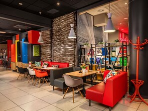 A modern cafe with red and black seating, wooden tables, and a variety of plants and books on shelves. - ibis Warszawa Centrum (Warsaw)