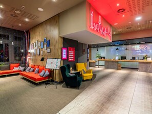 A modern hotel lobby with a reception desk, seating area with orange and green chairs, and a large neon sign. - ibis Warszawa Centrum (Warsaw)