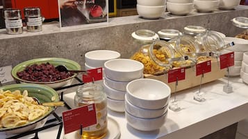 Un bufé con distintos alimentos, incluyendo tazones de cereal, un tarro de miel y recipientes con especias.