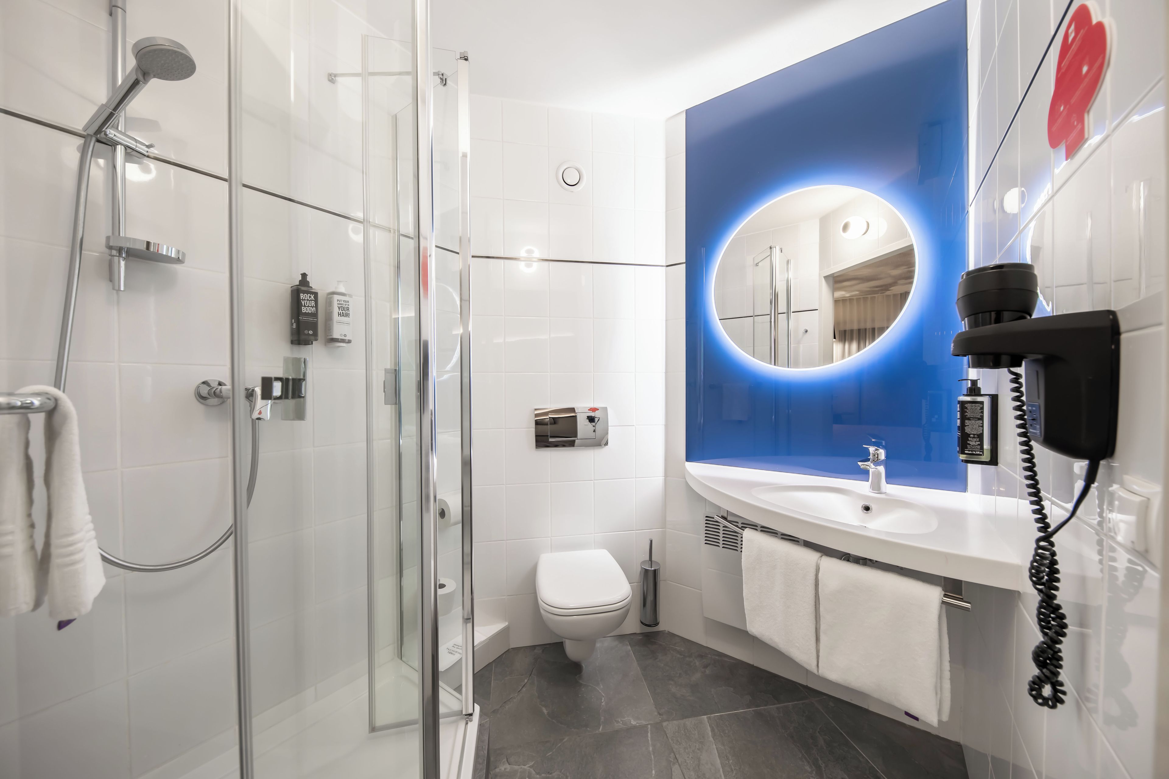 Une salle de bain moderne avec une douche à parois de verre, des toilettes blanches et un meuble-lavabo avec un miroir.