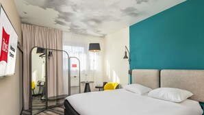 A hotel room with a bed, a desk, a chair, a lamp, and a view of the outside. - ibis Warszawa Centrum (Warsaw)