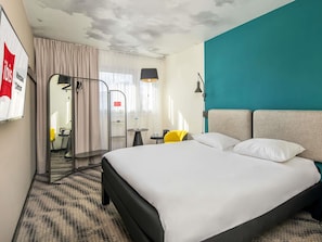 A hotel room with a bed, a desk, a chair, a lamp, and a view of the outside. - ibis Warszawa Centrum (Warsaw)