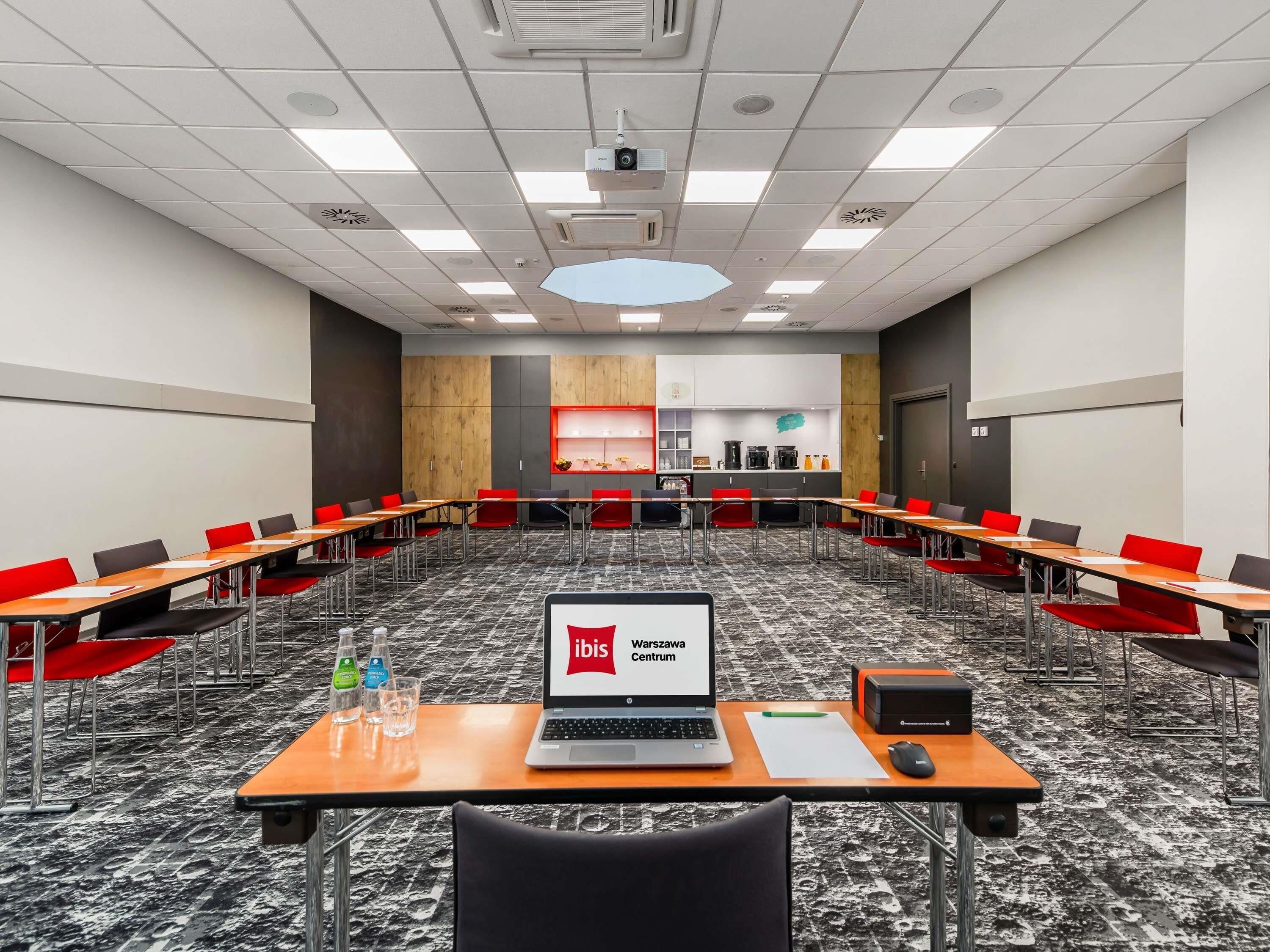 A conference room with a laptop displaying 'ibis Warszawa Centrum,' a projector, and a whiteboard.